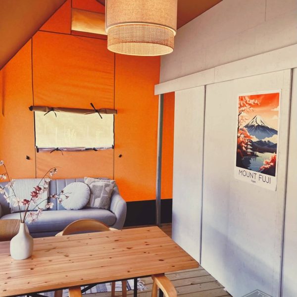 Coin salon lumineux et table à manger en bois avec une affiche du mont Fuji dans la tente safari « Fuji Rock » au Festilux Camp