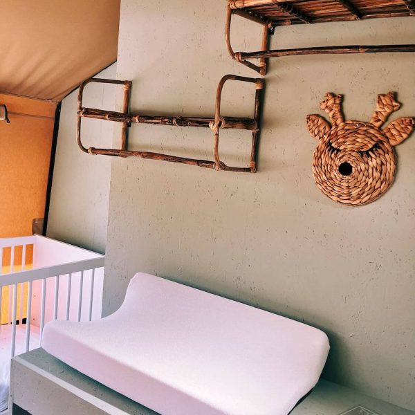 Chambre de bébé avec lit bébé, matelas à langer et étagères murales en rotin dans la tente safari Fuji Rock