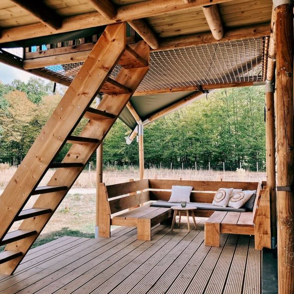 Véranda en bois de la tente safari Fuji Rock, avec banquette d'angle et escalier menant à la mezzanine, au Festilux Camp