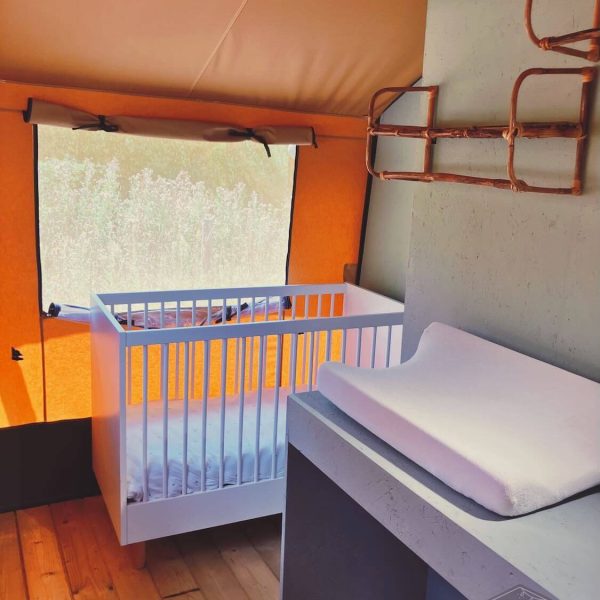 Chambre de bébé dans la tente safari Fuji Rock, avec un lit d'enfant blanc et une commode épurée équipée d'un matelas à langer