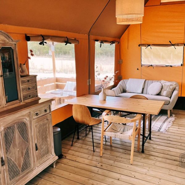 Spacieux espace de vie dans la tente safari Fuji Rock au Festilux Camp, avec coin salon, table à manger et armoire en bois