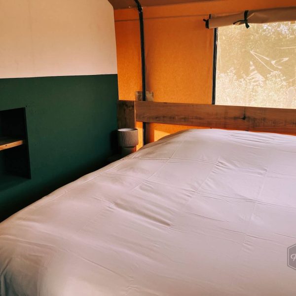 Lit double joliment aménagé, avec une tête de lit en bois et un mur vert, dans la tente safari Fuji Rock